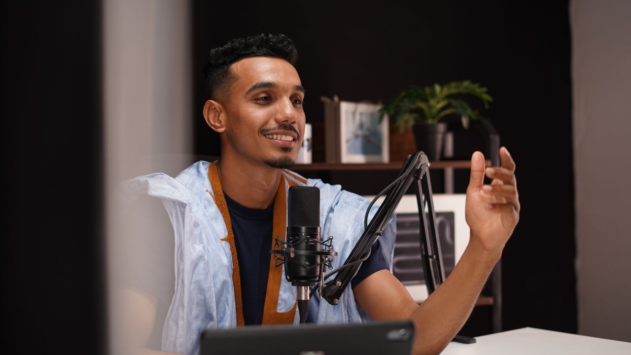 journey-01 Smiling young man recording a podcast in a cozy home studio with professional microphone setup.