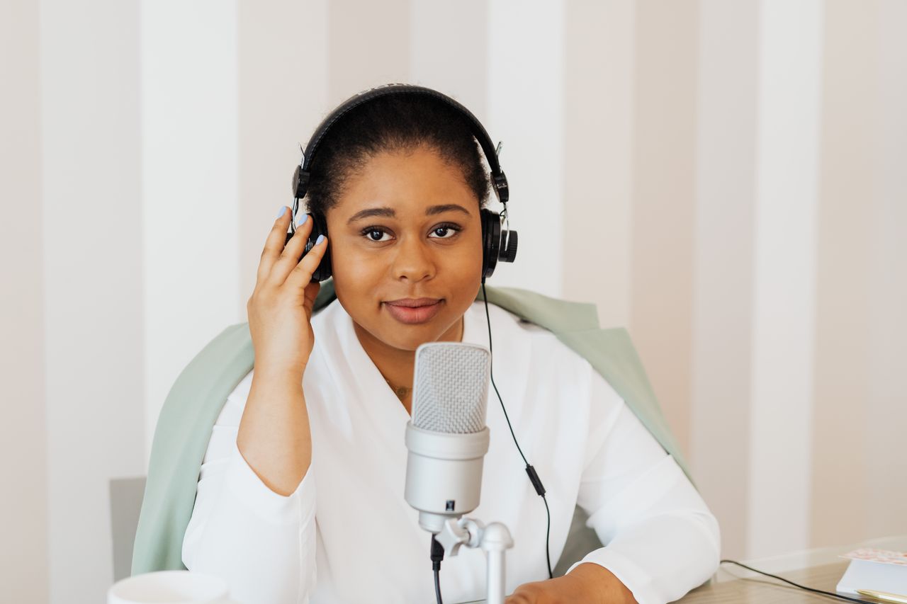 gallery-05 Young woman podcaster with headphones at a desk using a microphone.